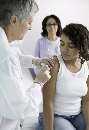 Un professionnel de la santé administre une injection dans le bras d'une fille. Une femme debout en arrière-plan.