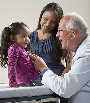Médico auscultando o tórax de uma menina com um estetoscópio, enquanto uma mulher observa.